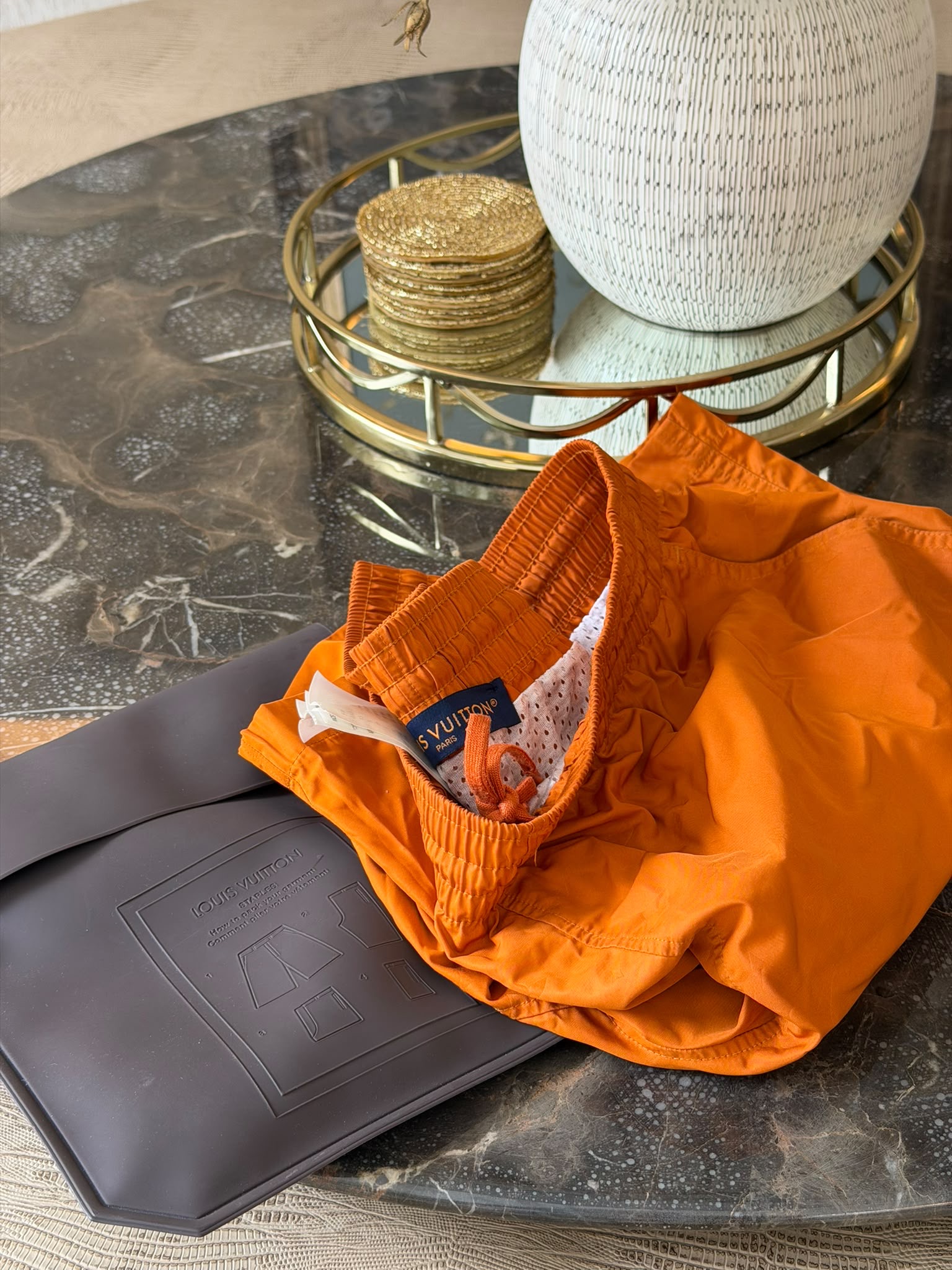 Engraved Louis Vuitton metal plaque on orange swim shorts
